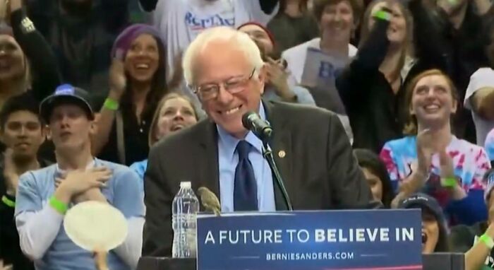 Bernie Sanders smiling at a bird on his podium, an unusual and wholesome political rally moment.