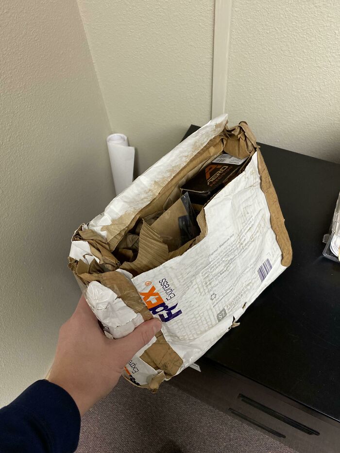 A hand holding a severely damaged FedEx package, a clear example of delivery fails that leave people speechless.