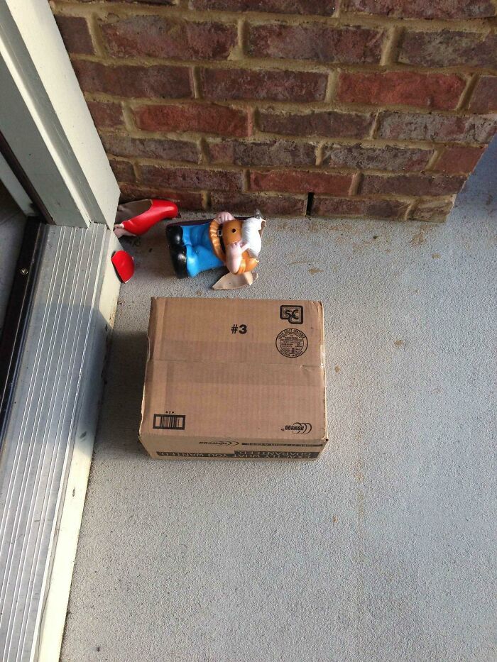 A small, intact delivery box sits on a porch, next to a shattered gnome, indicating a delivery fail.