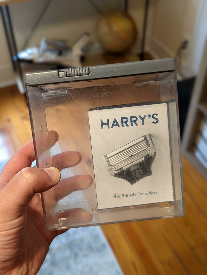 A hand holding an empty plastic box with a Harrys razor cartridge instruction manual inside, highlighting a delivery fail.