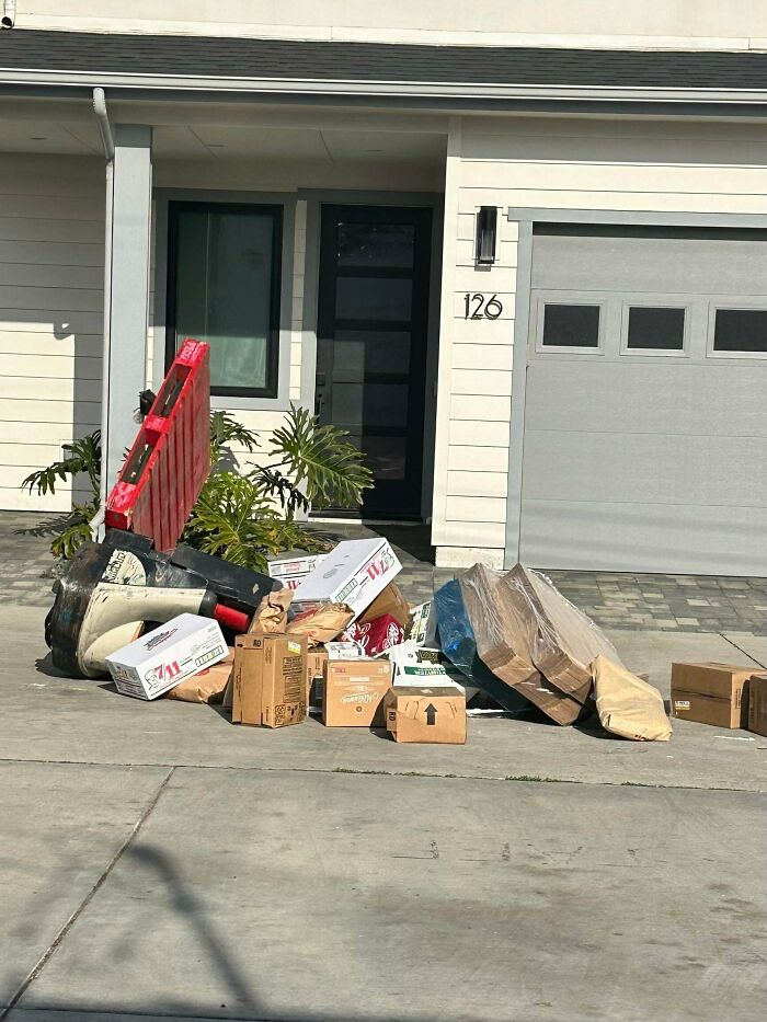 A large pile of various boxes and items dumped on a driveway in front of a house, highlighting delivery fails.