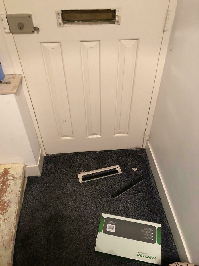 A mail slot broken off a white door with a package on the floor, showcasing delivery fails.
