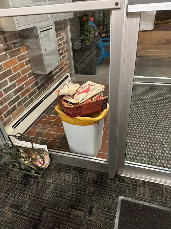 Pizza boxes and other food bags left on top of a trash can outside an apartment building, showing a delivery fail.