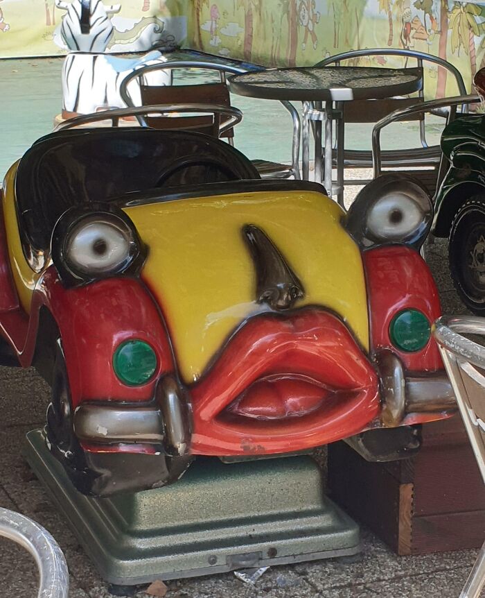 A creepy, yellow and red coin-operated kiddie car with large lips and eyes, a design fail.