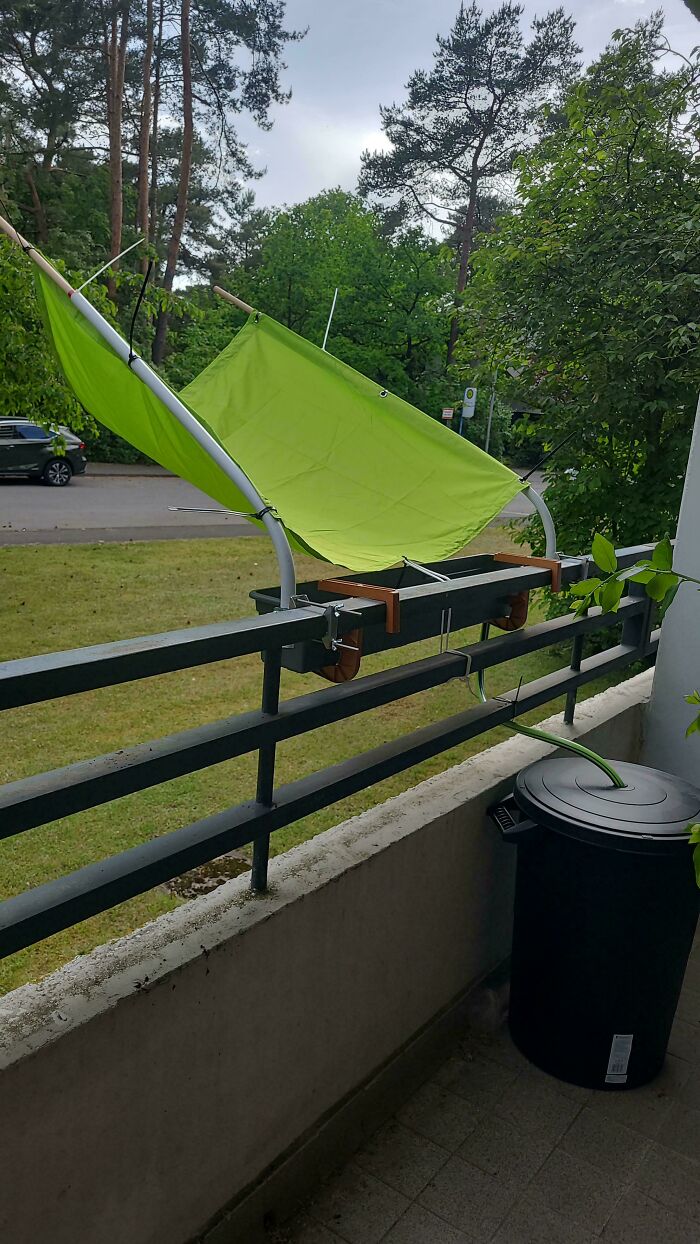 A bright green fabric sunshade rigged over a balcony railing, a clever solution for outdoor comfort.