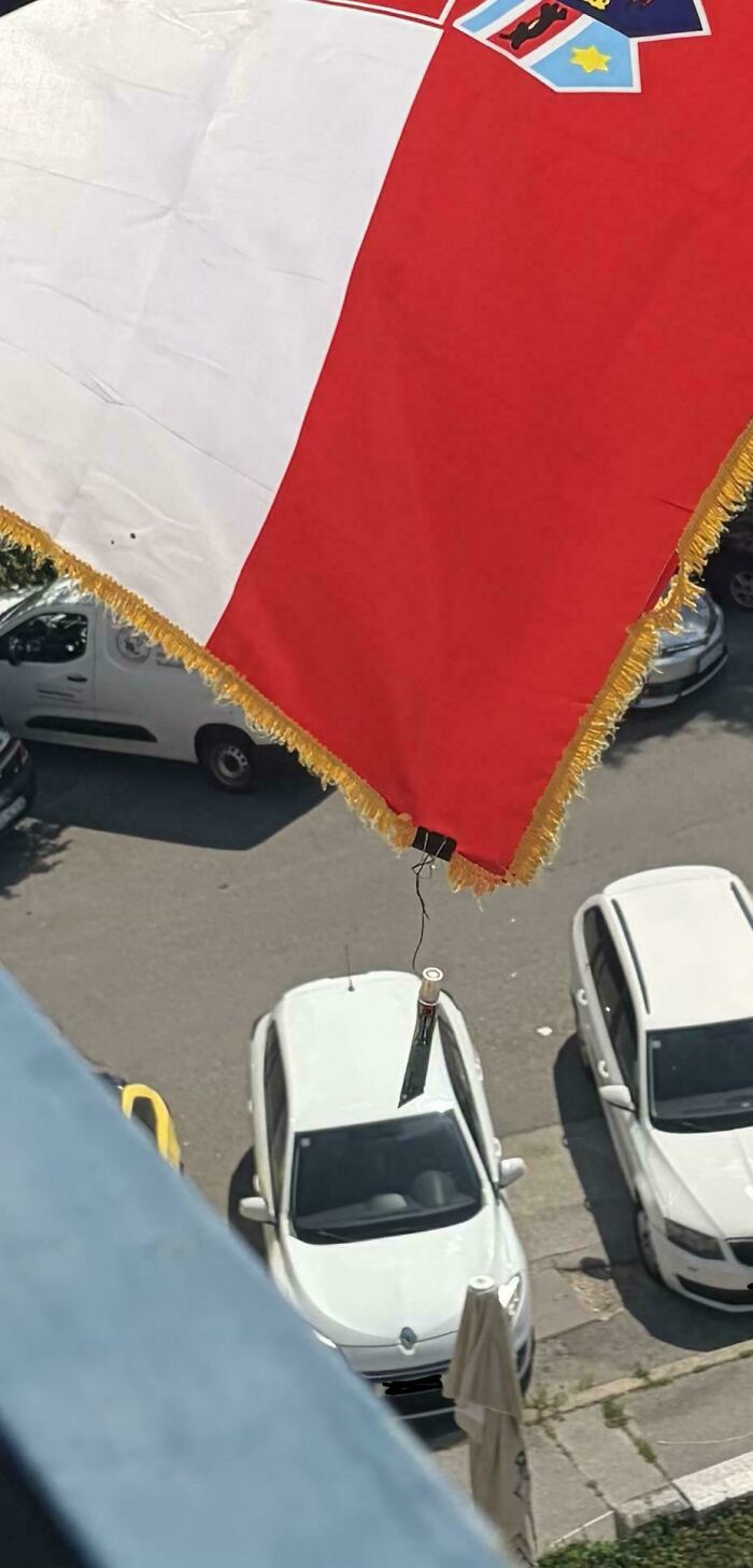 A large flag, red and white with a coat of arms, hanging over parked cars, a clever solution for display.