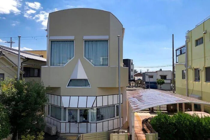 An unusual home designed to look like a skull, with window eyes and mouth, standing out in a suburban neighborhood.