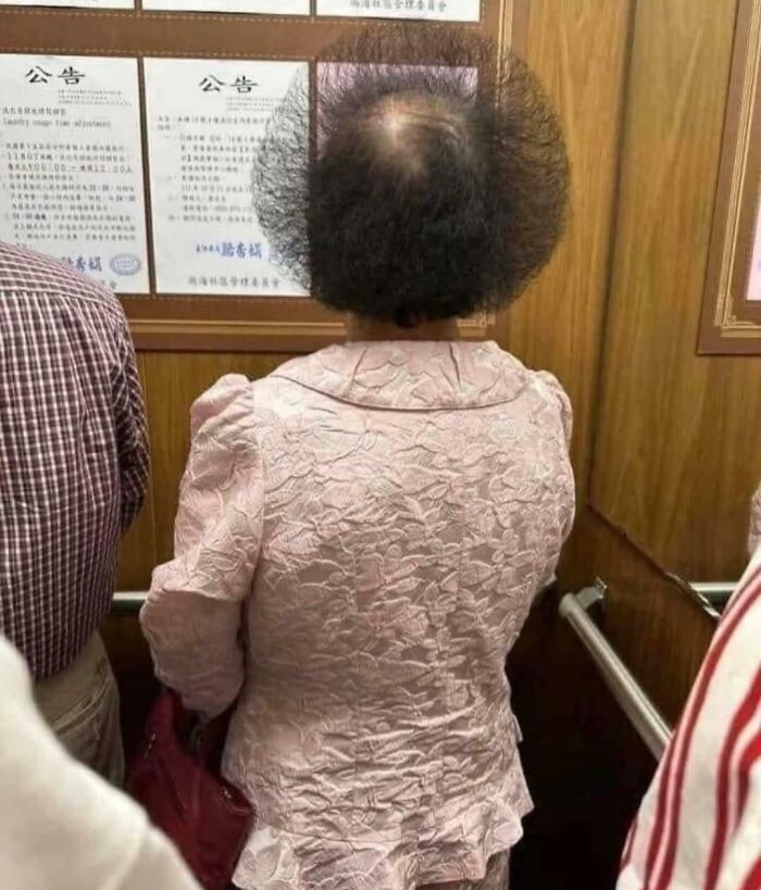Woman with unfortunate haircuts, showcasing a highly uneven circular cut from behind in an elevator.
