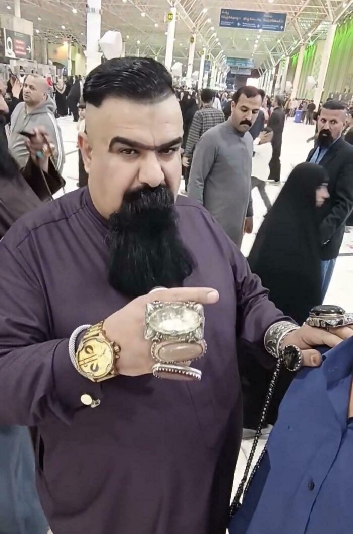 A man with a large beard, a unique shaved haircut, and many rings and bracelets on his hands.