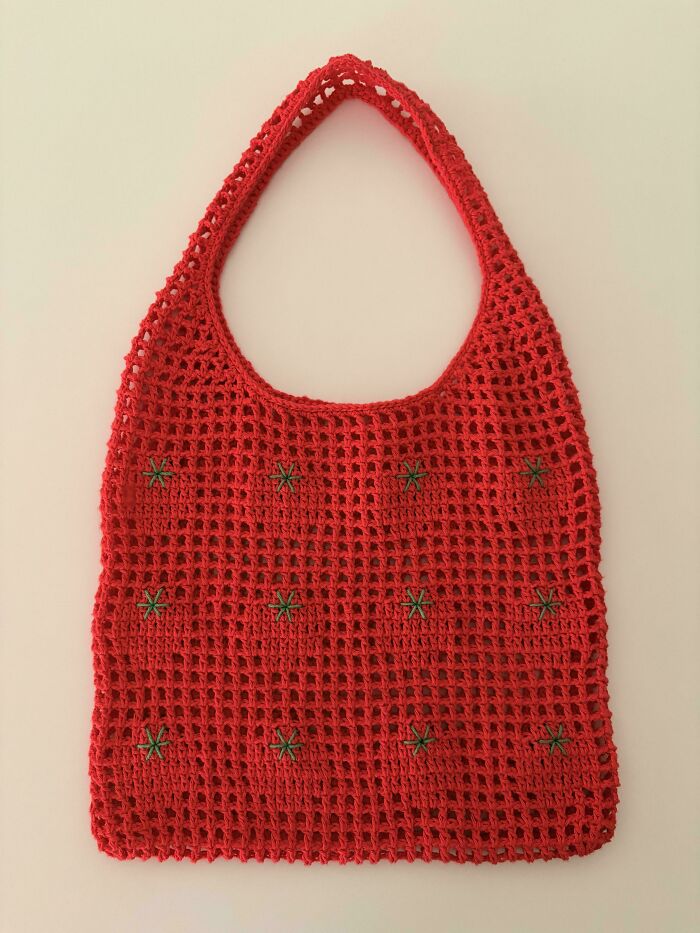 A red crochet bag with green flower details, an incredible example of crochet enthusiasm.