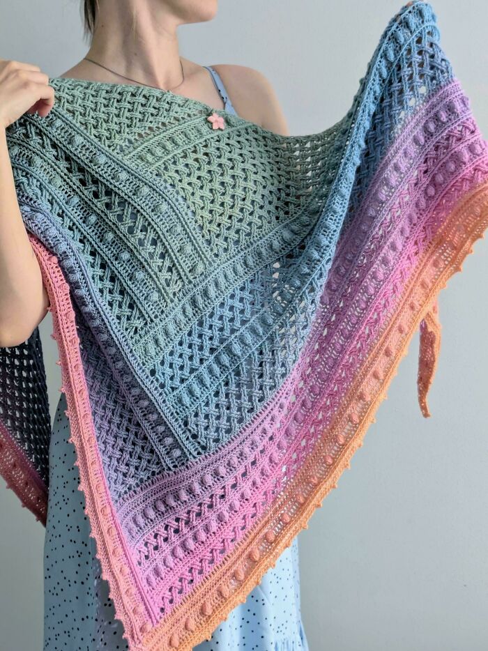 A woman holding a vibrant, multicolored crochet shawl, showcasing incredible crochet enthusiasm and artistry.