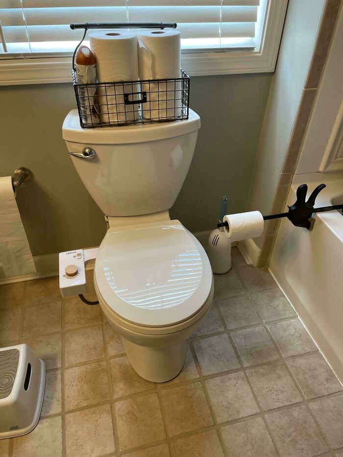 A toilet with a bidet attachment and a wire basket on top, showcasing a clever solution for bathroom organization.