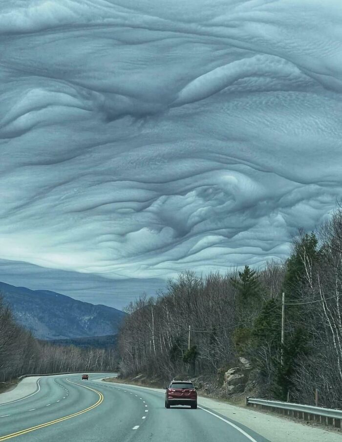 An interesting landscape with a winding road under fascinating, wavy cloud formations in a mountain setting