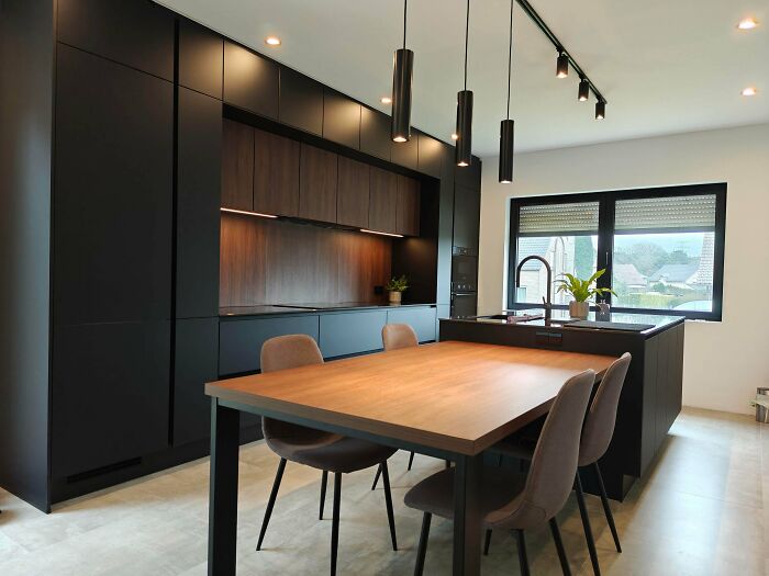Cool renovation of a modern kitchen with black cabinets, wooden accents, and a dining table.