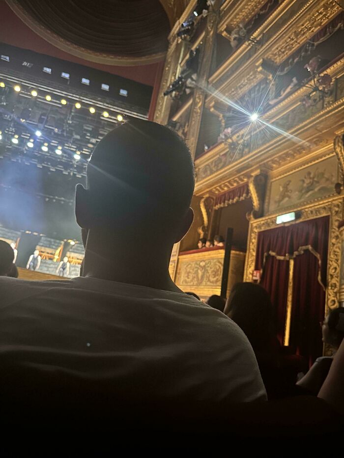 A concert attendee facing the stage, with a bright light directly behind their head, exemplifying a lack of basic human decency at an event.