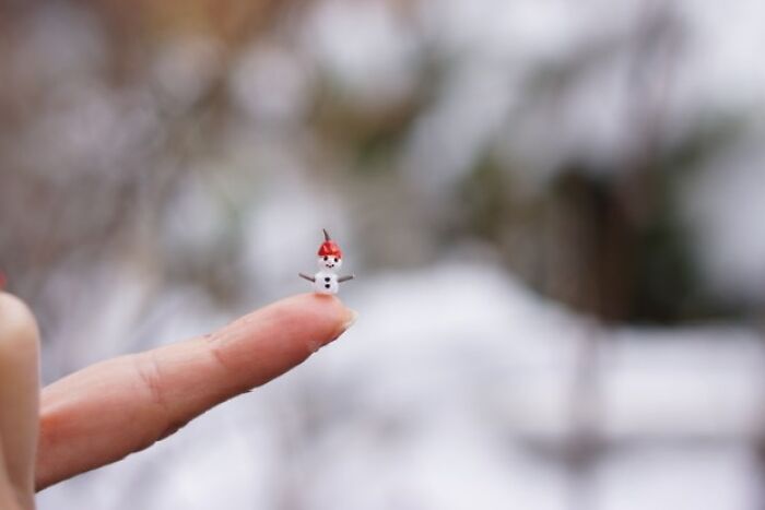 Miniature paper figure of a snowman with a red hat balancing on a fingertip.