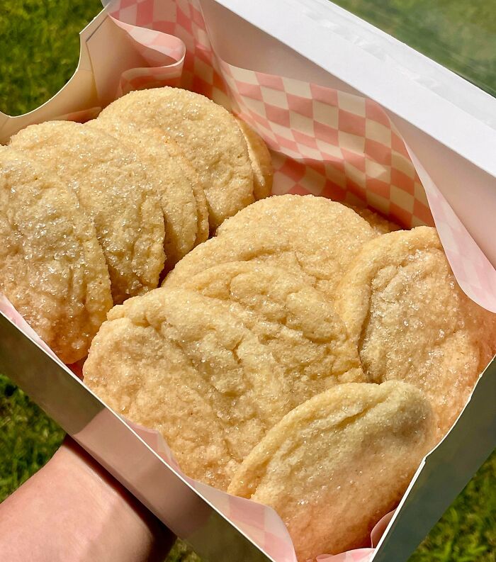 A hand holding a box filled with sugar-dusted baked treats, demonstrating a baker's delicious work.