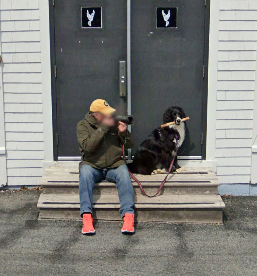 A bizarre Google Street View image of a person with a camera sitting on steps next to a dog holding a stick.