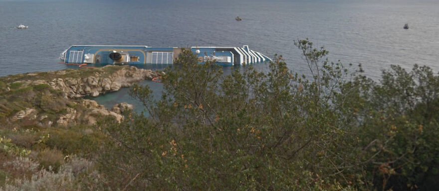 An aerial view of a capsized ship partially submerged near a rocky coastline, a bizarre scene captured in Google Street View photos.
