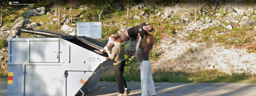 A funny Google Street View photo of three people with one being lifted above a large dumpster in a rocky, wooded area.
