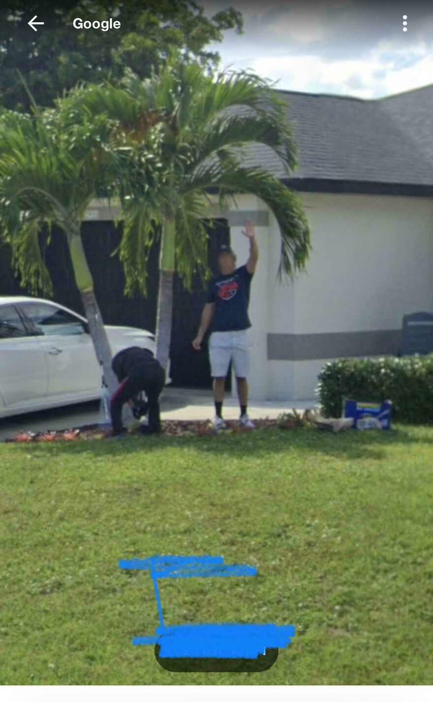 Two people working outside a house with palm trees, one reaching up, in a bizarre Google Street View image.