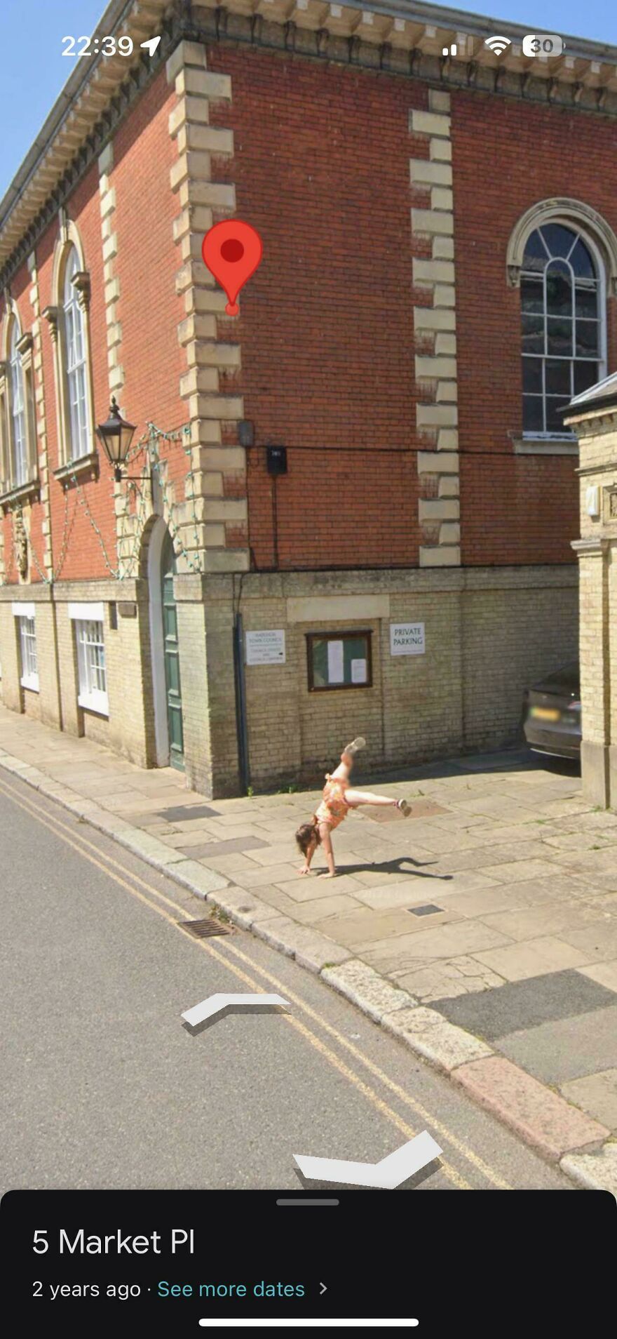 A person performing a handstand on a sidewalk next to a brick building, a bizarre Google Street View moment.