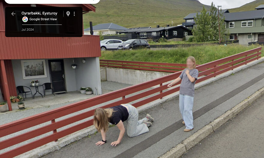 Two kids captured in a bizarre Google Street View photo, one crawling, the other pointing, on a residential street.