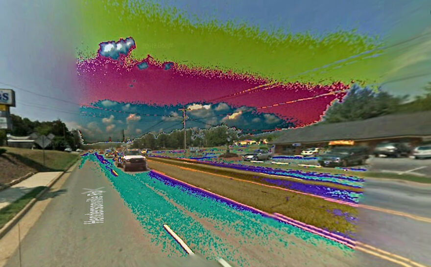 A glitchy Google Street View photo showing a road with distorted colors in the sky and foreground.
