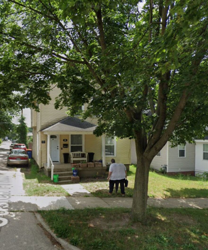 A person walks past a house, captured in a funny Google Street View photo, under a large tree.