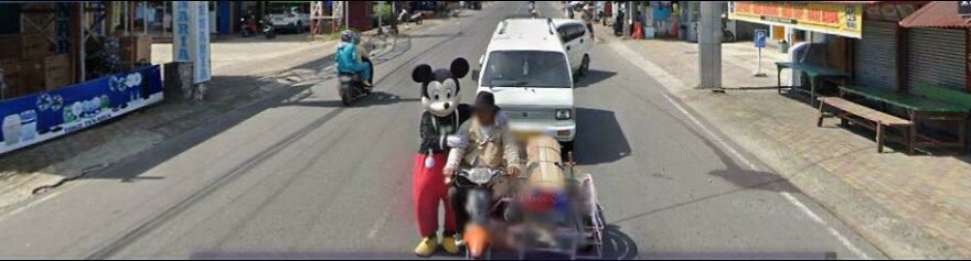 A Mickey Mouse character riding a scooter, captured in a bizarre Google Street View photo.