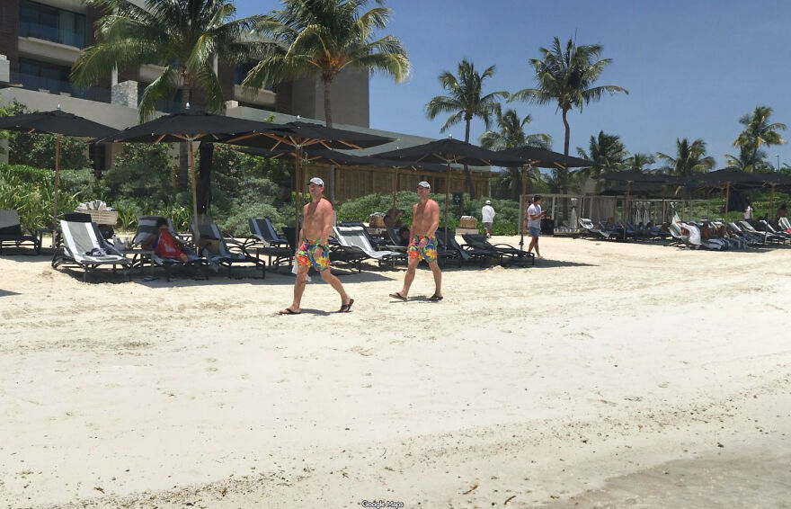 Two men in matching floral swim shorts walking on a sunny beach, captured in a bizarre Google Street View photo.