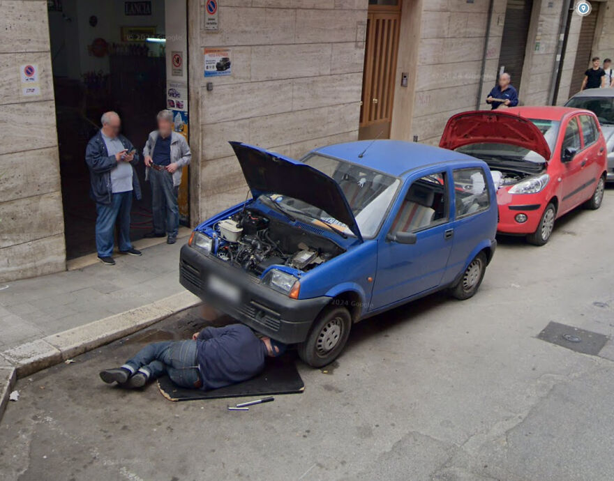 A person working under a small blue car, captured in a funny Google Street View photo.