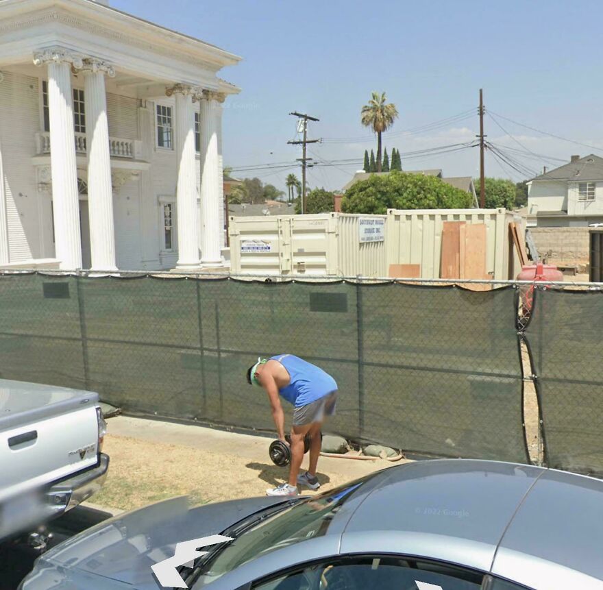 A funny Google Street View photo capturing a man doing a bizarre exercise with a dumbbell next to a white car.