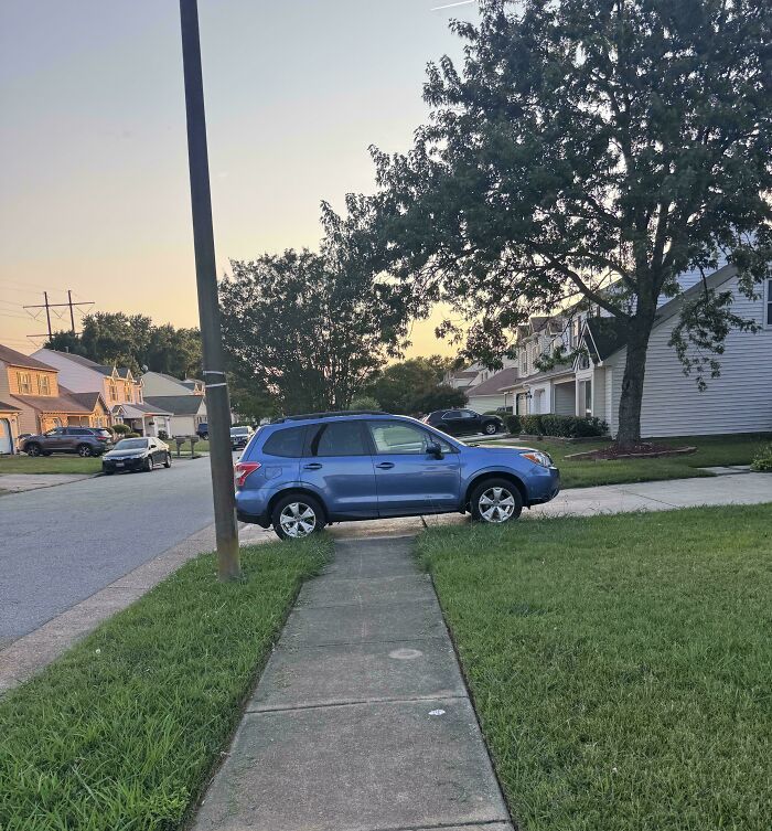 Blue SUV parked on a sidewalk and grass, displaying a lack of basic human decency in parking.