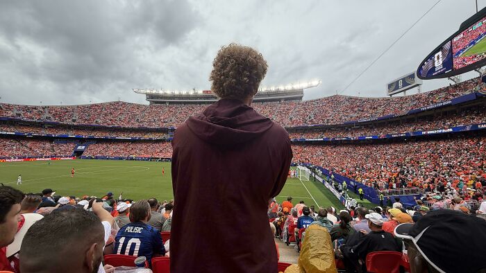 A person standing in a crowded soccer stadium, demonstrating a lack of basic human decency by obstructing view.