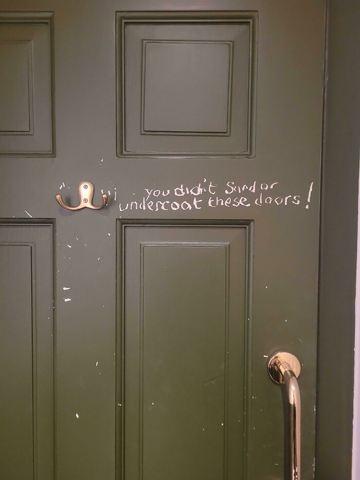 A scratched green door with white writing, indicating a disregard for basic human decency in maintenance.