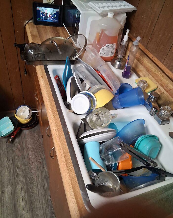 A kitchen sink overflowing with dirty dishes and cups, reflecting a disregard for basic human decency.