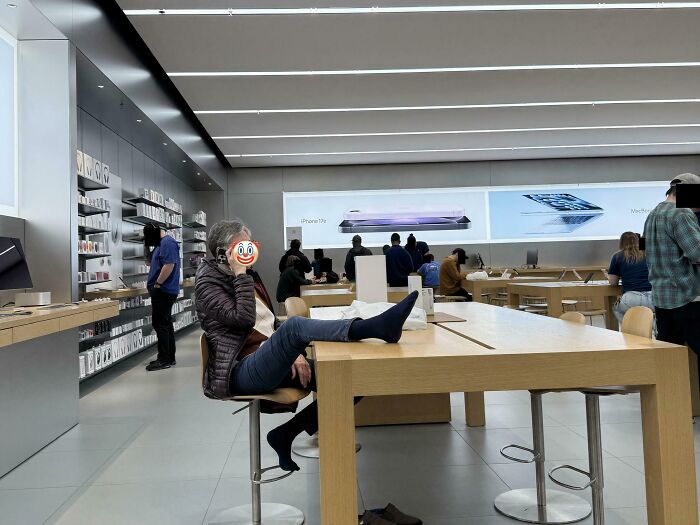 A person with feet on a table at an Apple store, displaying a disregard for basic human decency and public etiquette.
