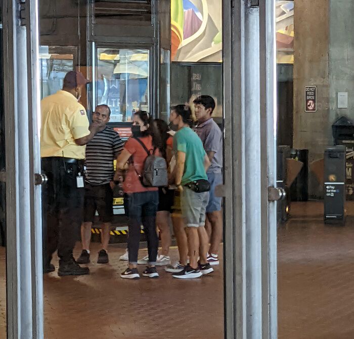 A group of people standing near an entrance, observing a situation that may involve a lack of basic human decency.