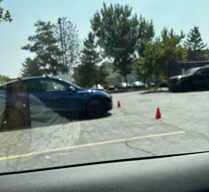 An out-of-focus image of a blue car and orange cones in a parking lot, representing a lapse in basic human decency.