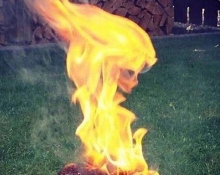 Flames taking the shape of a skull, rising from a fire pit on grass. A captivating 'When You See It' picture.