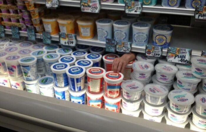 A person's hand reaching for yogurt in a refrigerated display. When You See It, the hand appears to emerge from within the shelf.