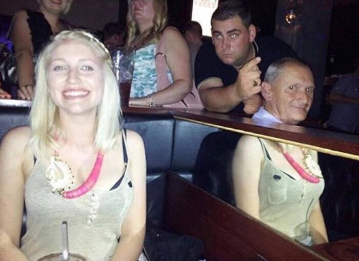 A girl smiling in a bar with a man's head appearing to be on the table. Another 'When You See It' picture.