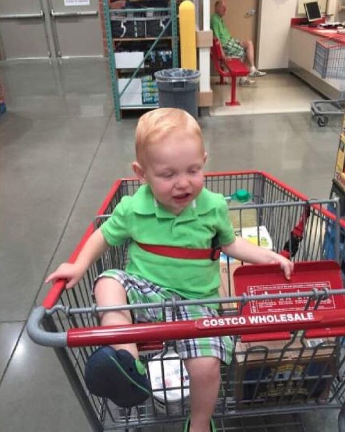 A young child sitting in a shopping cart in a Costco store. When You See It, a person in a green shirt is visible.
