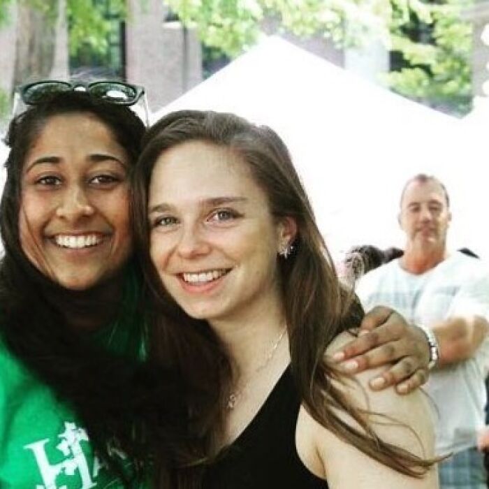 Two smiling women with a man in the background whose arm appears to be around the woman on the right, creating a When You See It picture.