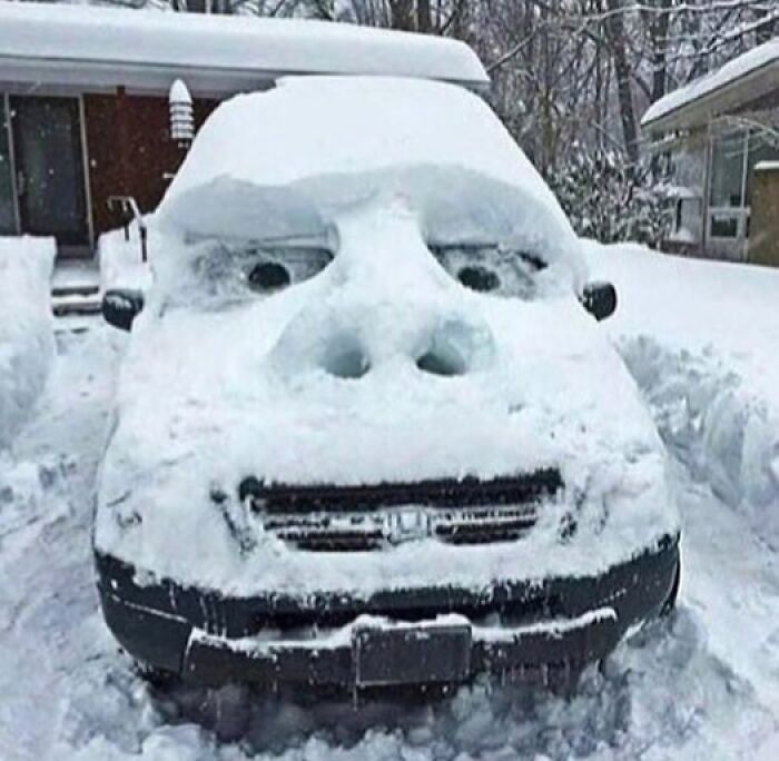 A car covered in snow, sculpted to look like a surprised face, an amusing when you see it picture.