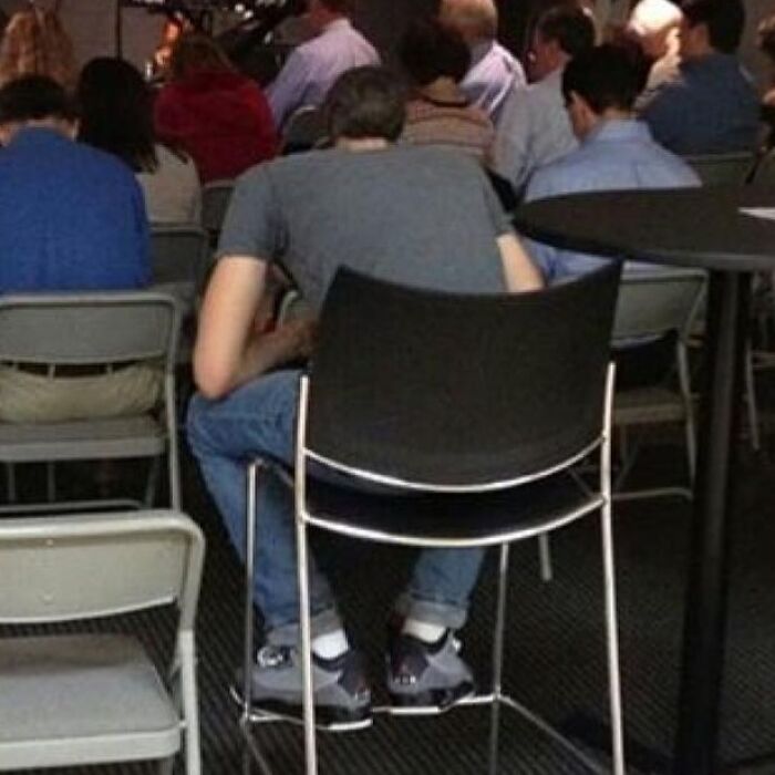 A person sitting on a chair that is stacked on another chair, a puzzling when you see it picture.