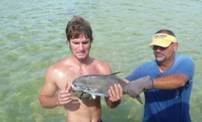 A man holding a fish in water with another man looking on, an example of When You See It Pictures.