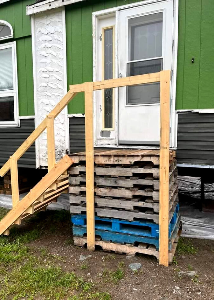 A makeshift front porch made from stacked wooden pallets and a new wooden railing, a clever solution.