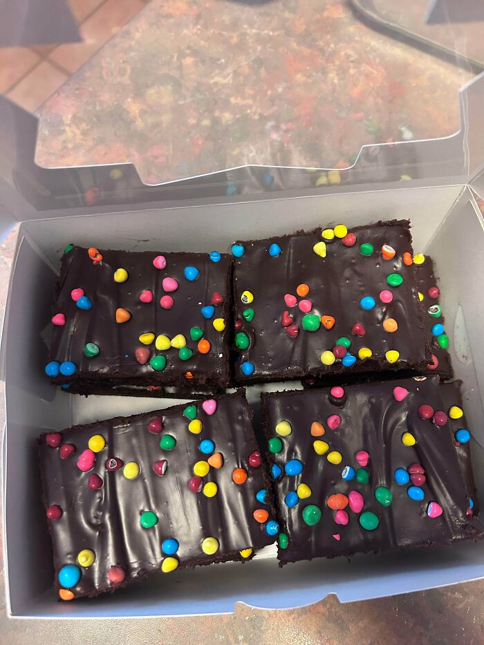 Four decadent chocolate brownies covered in colorful sprinkles, presented in a box, highlighting bakers delicious treats.